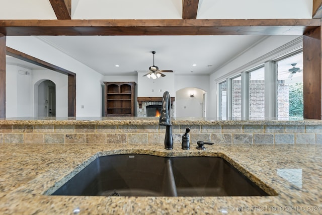 kitchen featuring tasteful backsplash, light stone counters, ornamental molding, sink, and beamed ceiling