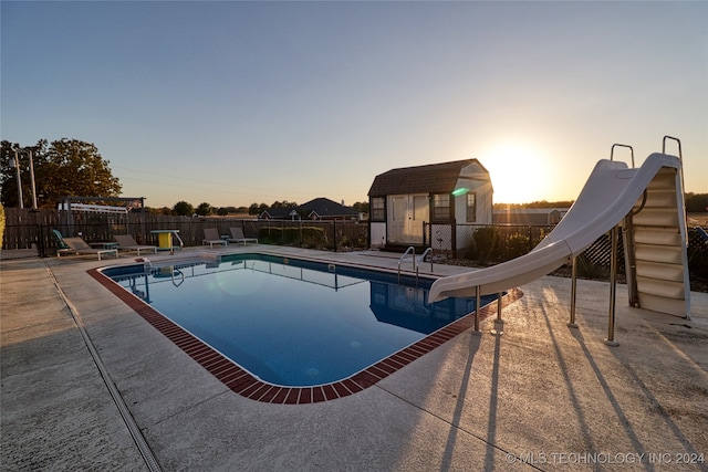 pool at dusk featuring a patio, a storage shed, and a water slide