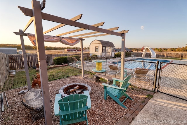 pool at dusk featuring a storage unit, a pergola, an outdoor fire pit, and a water slide