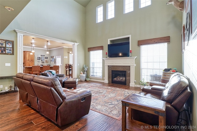 living room with decorative columns, a towering ceiling, dark wood-type flooring, and ornamental molding