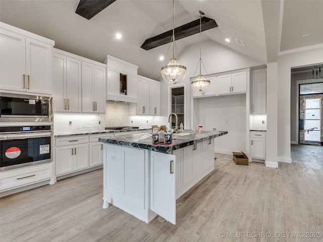 kitchen featuring white cabinetry, an island with sink, appliances with stainless steel finishes, decorative light fixtures, and vaulted ceiling with beams