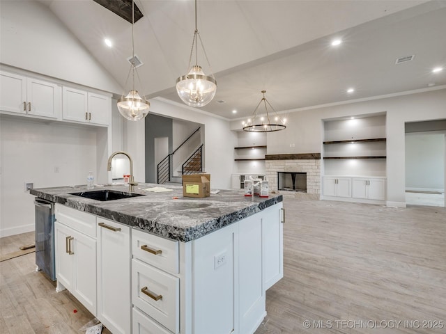 kitchen with pendant lighting, built in shelves, white cabinetry, sink, and a center island with sink