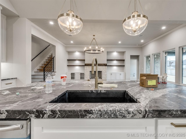 kitchen with dark stone countertops, pendant lighting, sink, crown molding, and white cabinets