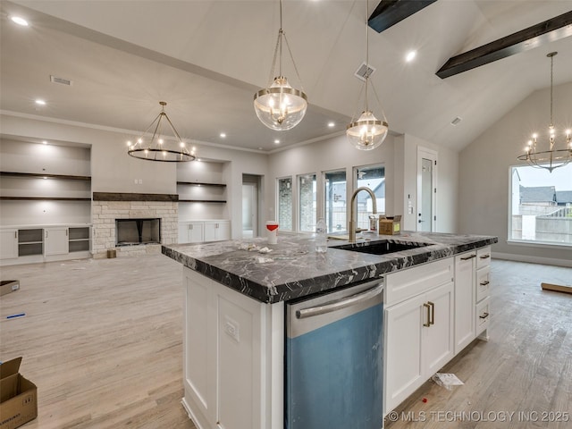 kitchen featuring pendant lighting, stainless steel dishwasher, a center island with sink, sink, and built in shelves