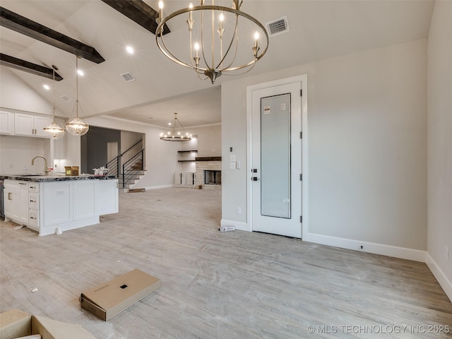 kitchen featuring lofted ceiling with beams, white cabinets, hanging light fixtures, and a notable chandelier