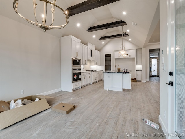 kitchen with stainless steel appliances, hanging light fixtures, a kitchen island, white cabinets, and beamed ceiling