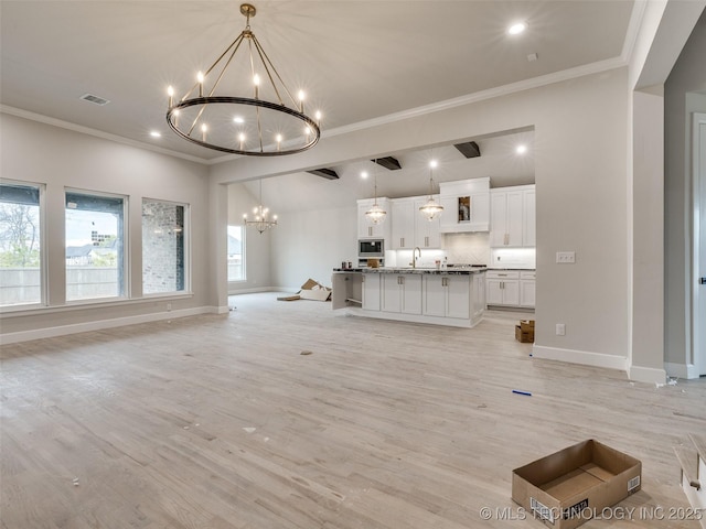 unfurnished living room featuring sink, light hardwood / wood-style flooring, ornamental molding, and a notable chandelier