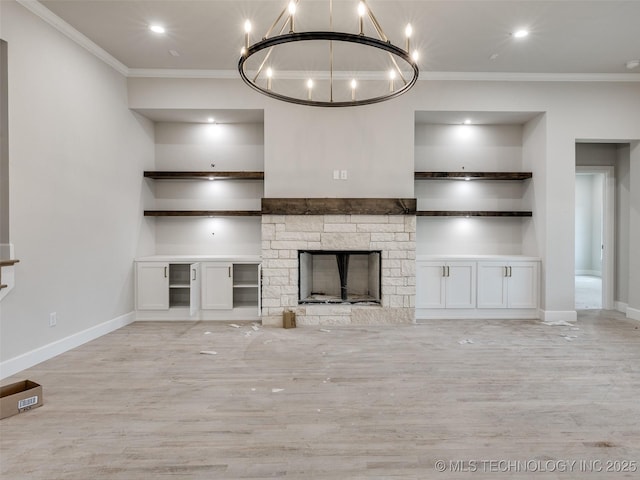 unfurnished living room with built in features, crown molding, a stone fireplace, and a notable chandelier