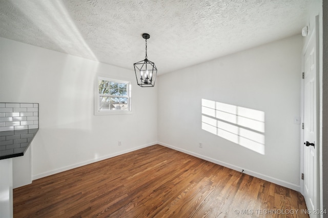 unfurnished dining area with a textured ceiling, dark hardwood / wood-style floors, and a notable chandelier