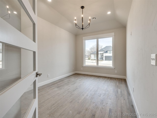 spare room featuring lofted ceiling, a chandelier, and light wood-type flooring