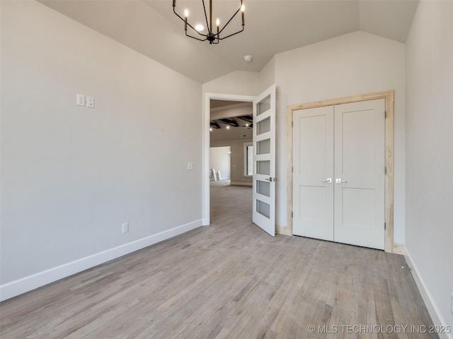 unfurnished bedroom featuring lofted ceiling, light hardwood / wood-style flooring, a closet, and a notable chandelier