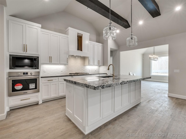 kitchen with appliances with stainless steel finishes, an island with sink, vaulted ceiling with beams, white cabinets, and hanging light fixtures