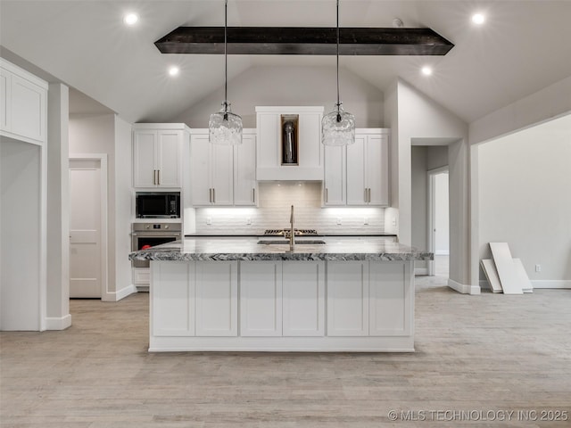 kitchen featuring decorative light fixtures, black microwave, a center island with sink, oven, and white cabinets