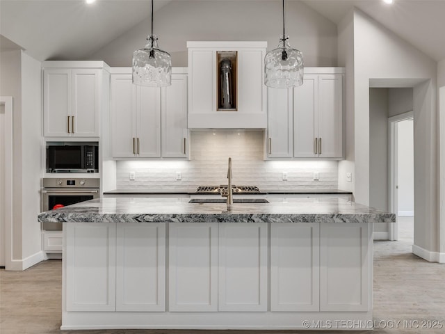 kitchen with appliances with stainless steel finishes, decorative light fixtures, and an island with sink