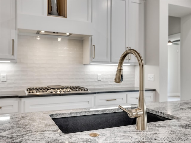 kitchen featuring tasteful backsplash, sink, white cabinets, dark stone counters, and stainless steel gas cooktop