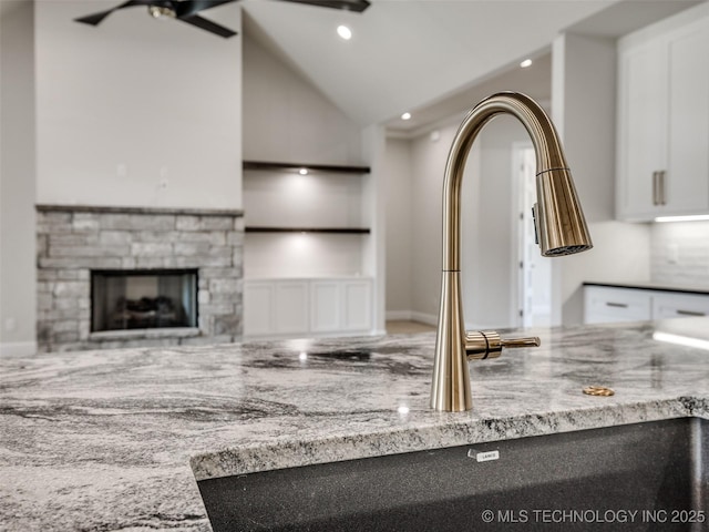 kitchen featuring lofted ceiling, sink, white cabinetry, light stone counters, and a stone fireplace