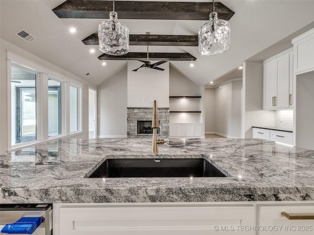 kitchen with lofted ceiling with beams, white cabinetry, sink, and a fireplace