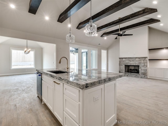 kitchen featuring sink, white cabinetry, light stone counters, decorative light fixtures, and a center island with sink