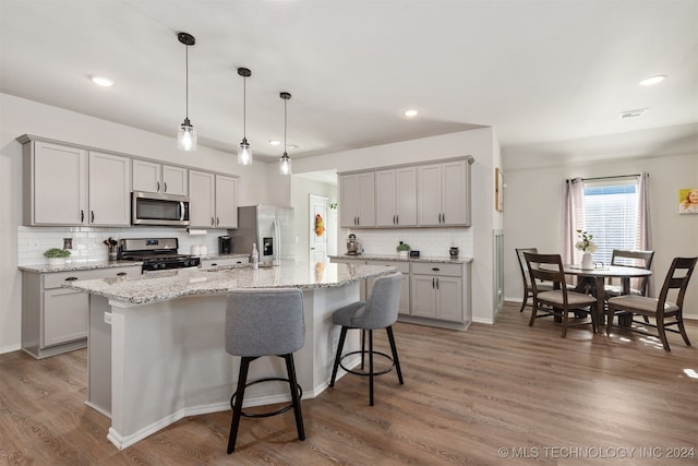 kitchen with hanging light fixtures, a center island with sink, stainless steel appliances, and wood-type flooring