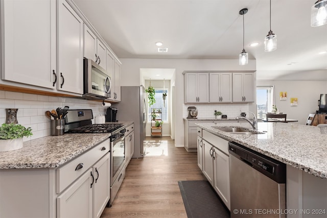 kitchen with light stone countertops, sink, hanging light fixtures, light hardwood / wood-style flooring, and appliances with stainless steel finishes