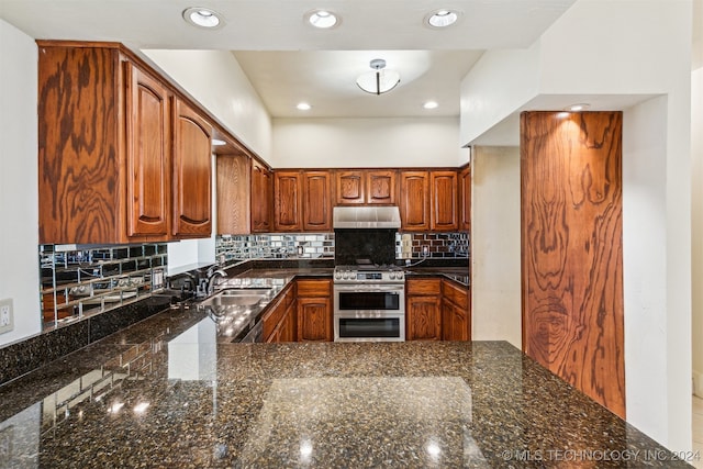 kitchen featuring decorative backsplash, dark stone countertops, stainless steel range with gas cooktop, and sink