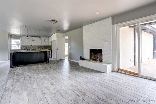 unfurnished living room with a fireplace, sink, and light wood-type flooring