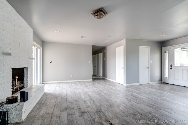 unfurnished living room featuring hardwood / wood-style floors and a brick fireplace