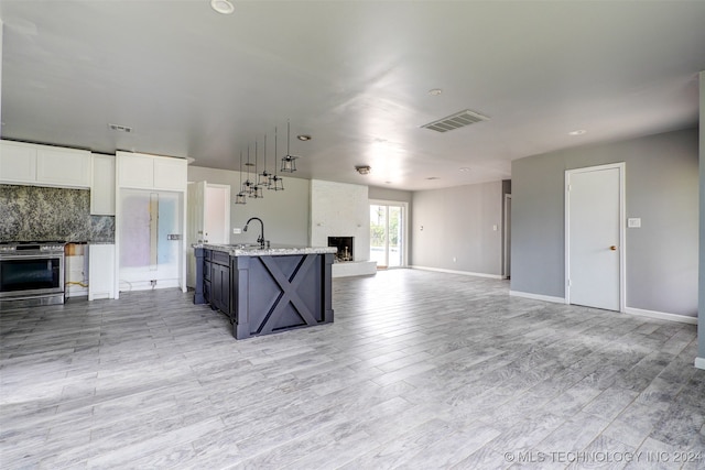 kitchen featuring light wood-type flooring, backsplash, a kitchen island with sink, sink, and white cabinetry