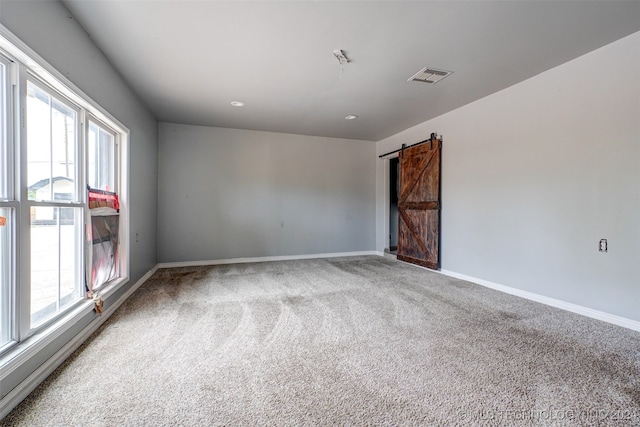 unfurnished room featuring carpet, plenty of natural light, and a barn door