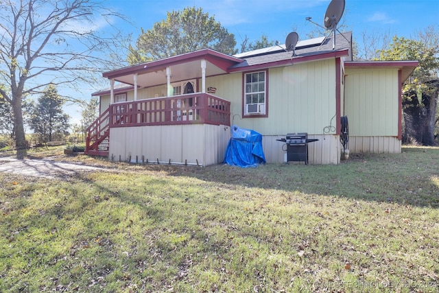 rear view of property featuring solar panels, a wooden deck, and a lawn