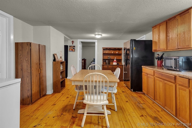 kitchen with black fridge, a textured ceiling, light hardwood / wood-style flooring, and fridge