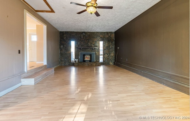 unfurnished living room featuring light hardwood / wood-style floors, a stone fireplace, and a textured ceiling