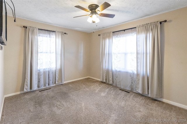 carpeted empty room with ceiling fan, a textured ceiling, and a wealth of natural light