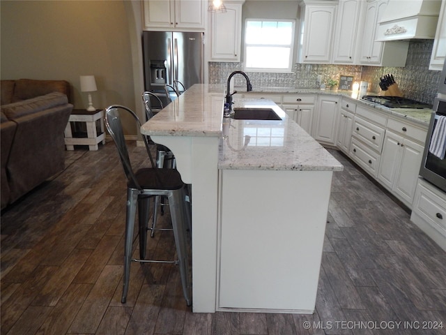 kitchen featuring sink, an island with sink, decorative backsplash, custom range hood, and appliances with stainless steel finishes