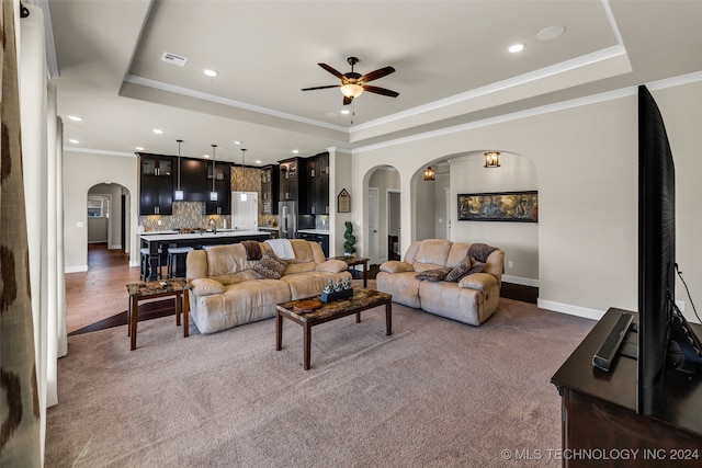 carpeted living room featuring ceiling fan, a raised ceiling, and ornamental molding