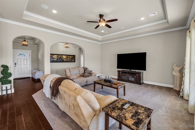 living room with ceiling fan with notable chandelier, dark hardwood / wood-style flooring, ornamental molding, and a tray ceiling