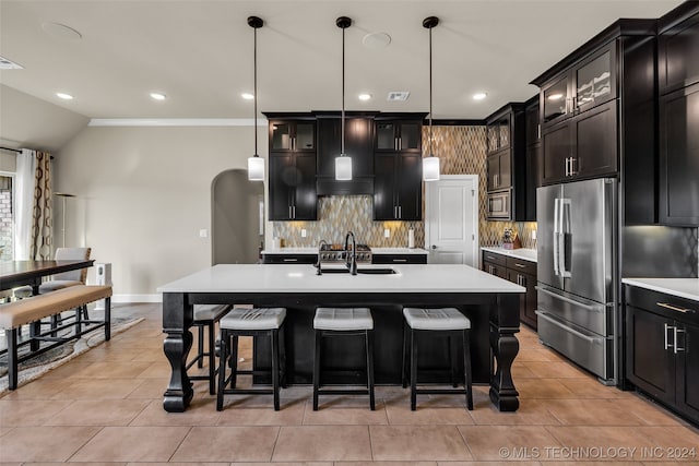 kitchen featuring a center island with sink, sink, appliances with stainless steel finishes, tasteful backsplash, and decorative light fixtures