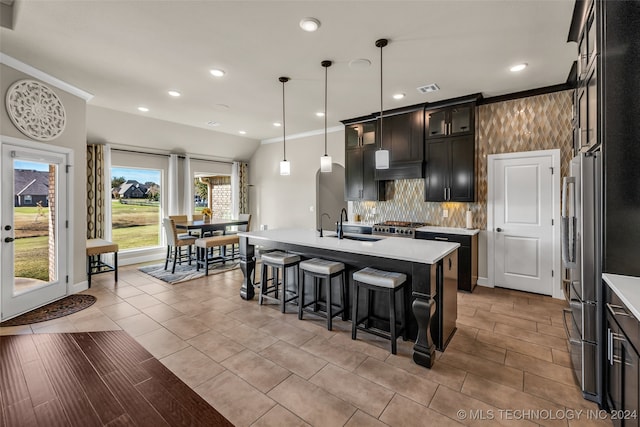 kitchen with sink, stainless steel appliances, crown molding, pendant lighting, and a center island with sink