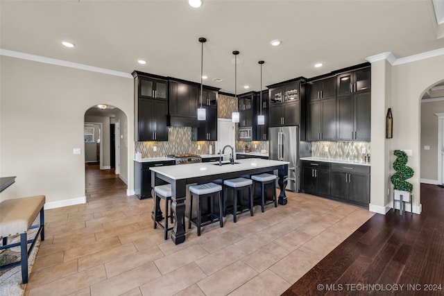 kitchen featuring light wood-type flooring, ornamental molding, stainless steel appliances, pendant lighting, and an island with sink