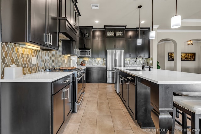 kitchen with backsplash, a center island with sink, crown molding, appliances with stainless steel finishes, and decorative light fixtures