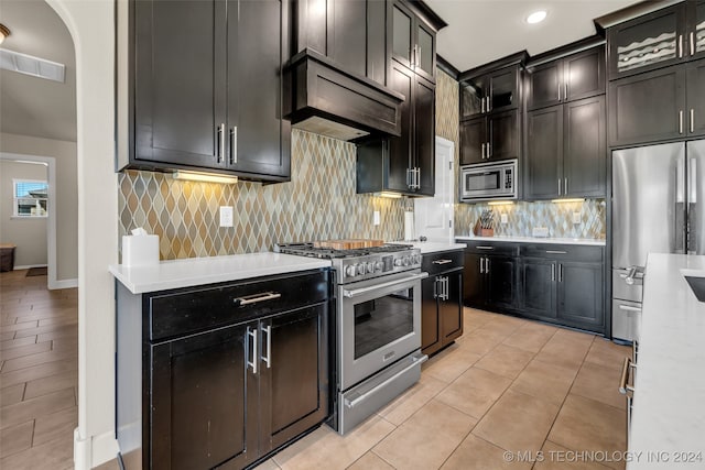 kitchen with light tile patterned flooring, premium range hood, stainless steel appliances, and tasteful backsplash