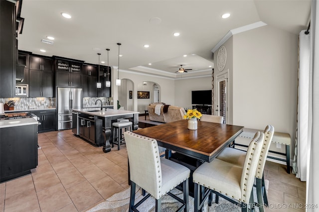 tiled dining area featuring ceiling fan, ornamental molding, sink, and a tray ceiling