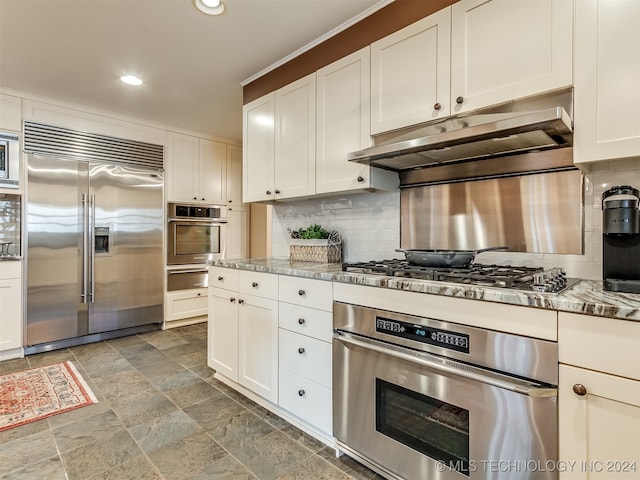 kitchen with white cabinetry, backsplash, light stone counters, and stainless steel appliances