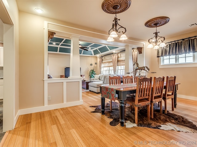 dining room with ceiling fan with notable chandelier, hardwood / wood-style flooring, and ornate columns