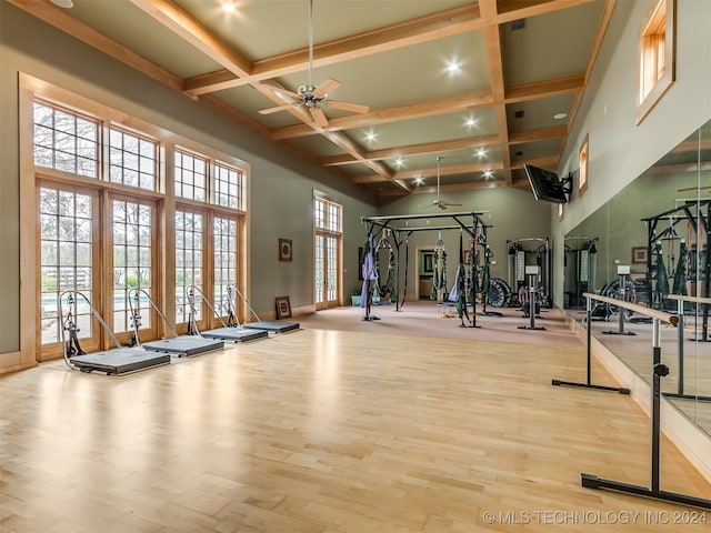 workout area with ceiling fan, a towering ceiling, coffered ceiling, and light wood-type flooring