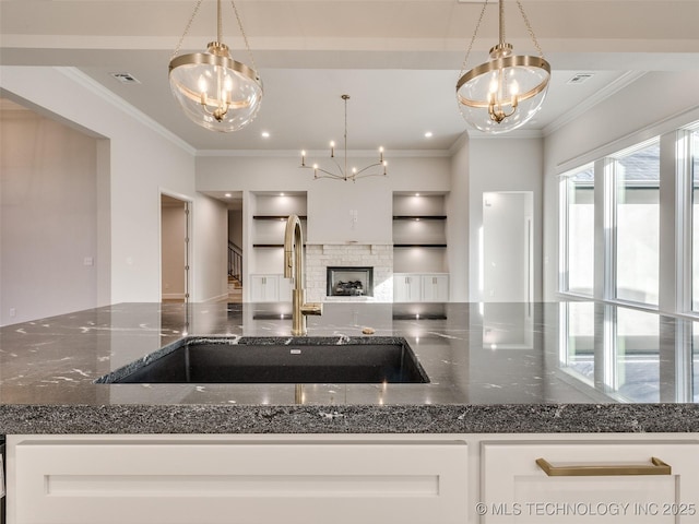 kitchen with dark stone countertops, an inviting chandelier, a sink, open floor plan, and crown molding