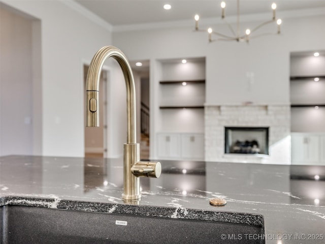 details featuring dark stone countertops, an inviting chandelier, ornamental molding, a fireplace, and built in features