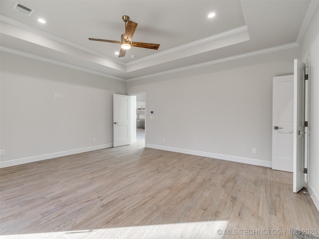 spare room with visible vents, light wood-style floors, a tray ceiling, ornamental molding, and a ceiling fan
