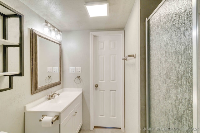 bathroom with vanity, a shower with shower door, and a textured ceiling