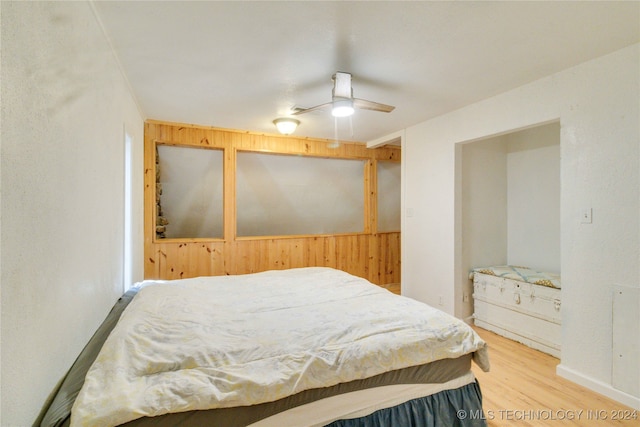 bedroom with hardwood / wood-style flooring, ceiling fan, and wooden walls